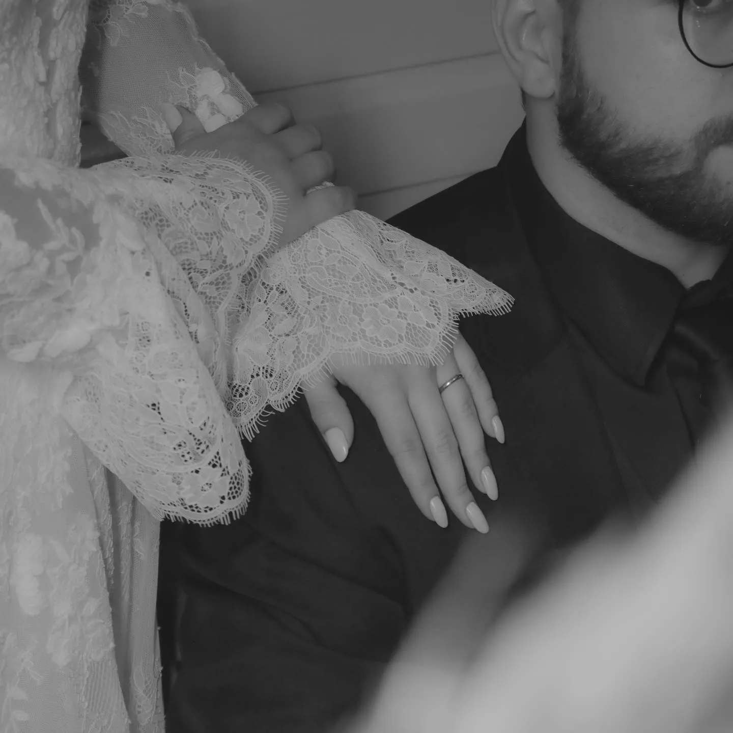 Mãos dos noivos com aliança e renda do vestido, em preto e branco