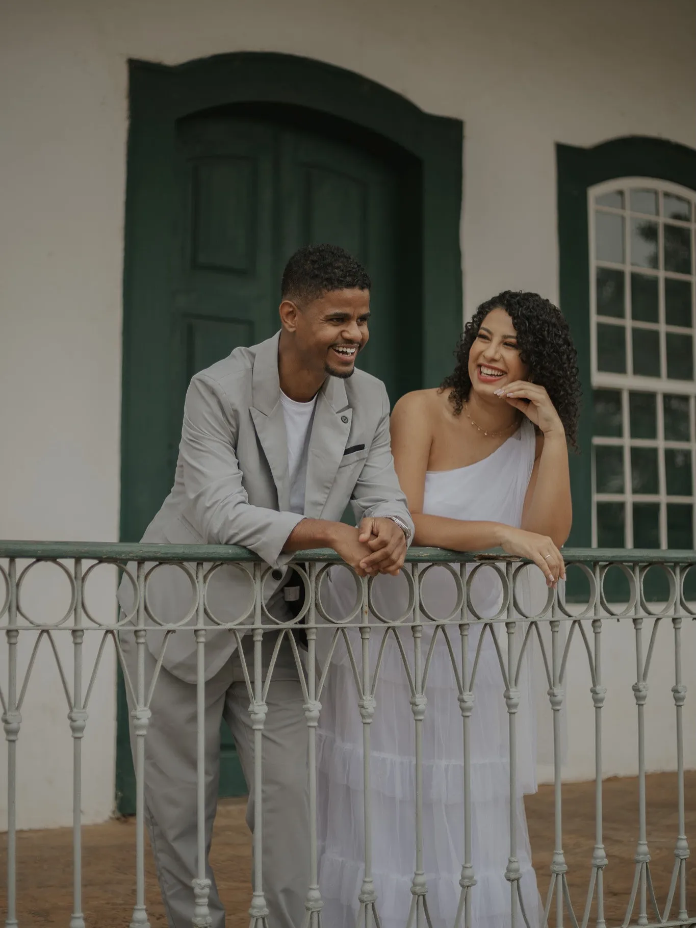 Casal rindo apoiado em uma sacada de ferro de casarão colonial